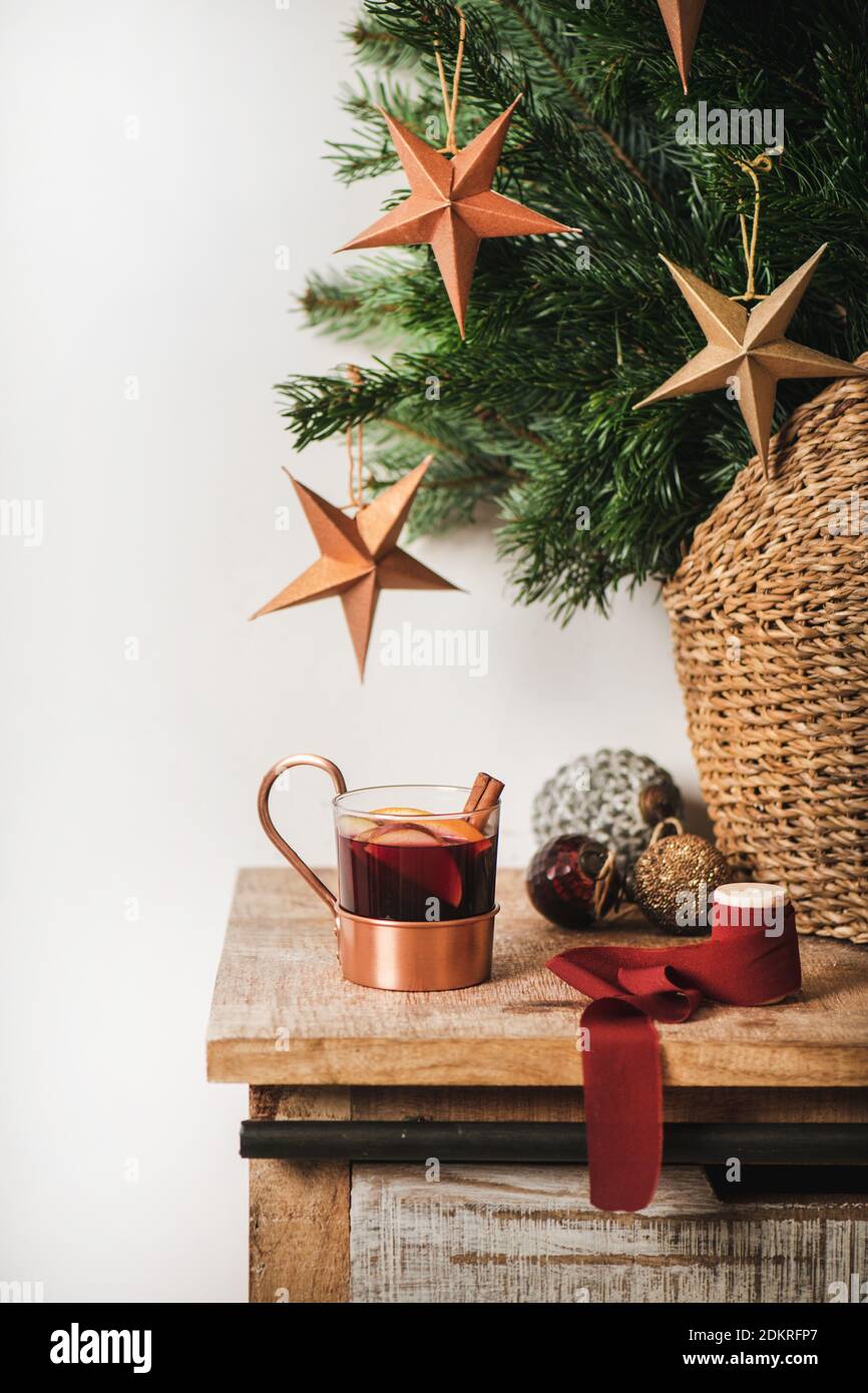 Cup of mulled wine over wooden kitchen counter with Christmas festive decorative baubles and stars and Christmas tree branches at background. Winter holiday mood concept Stock Photo