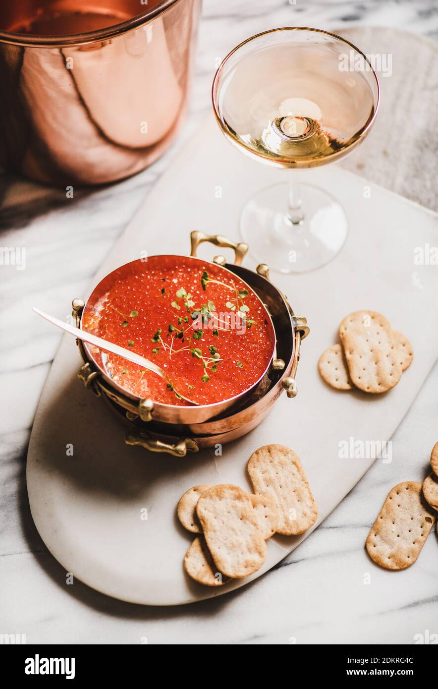 Red caviar in copper metal dishes with salty crackers and glass of champaigne over white marble table, top view. Winter holiday mood concept Stock Photo