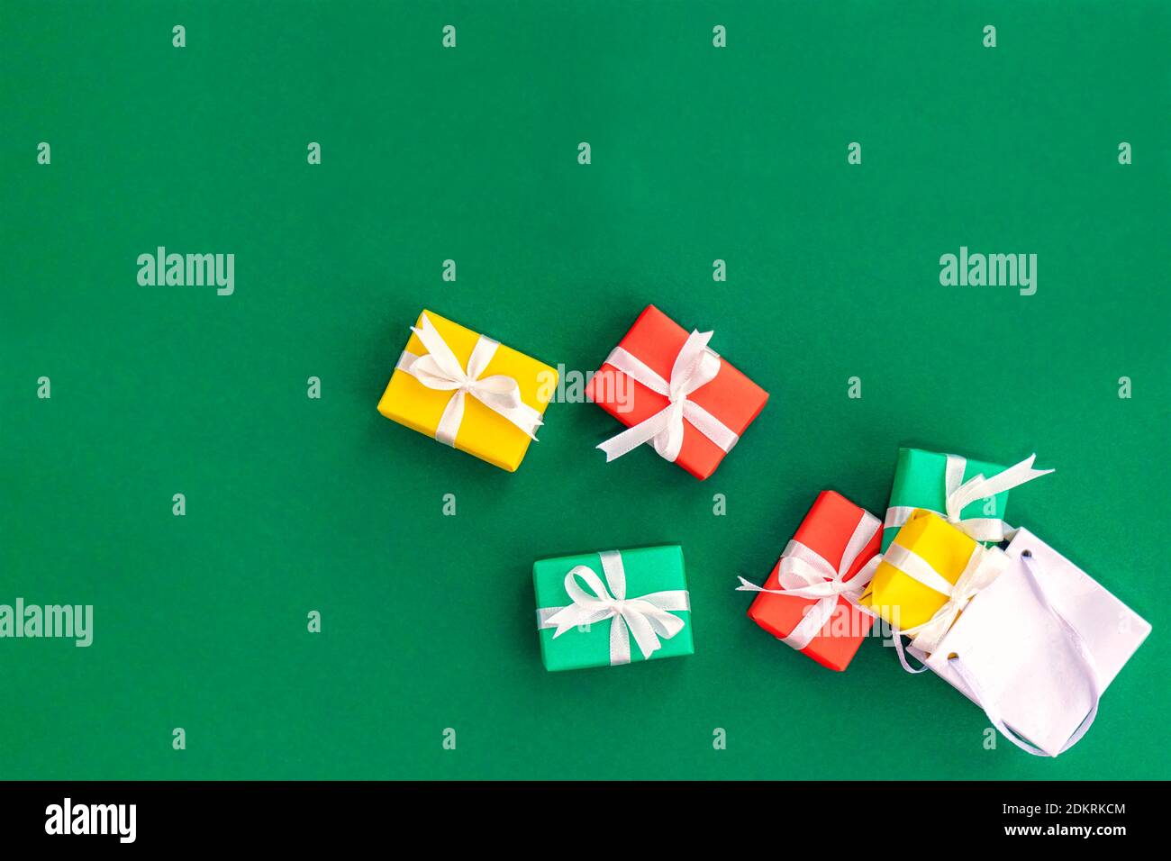 Fallen paper bag with scattered gifts. Red, green and yellow gifts in a shopping bag on a green background with space for text. Christmas and Xmas gif Stock Photo