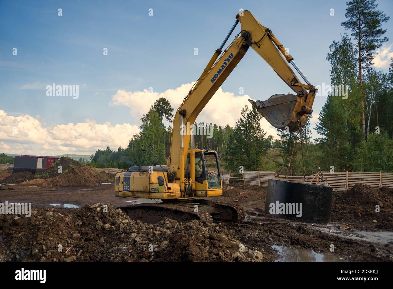 The excavator is carrying a concrete ring to install a sewer well in a pipeline at a construction site. Stock Photo