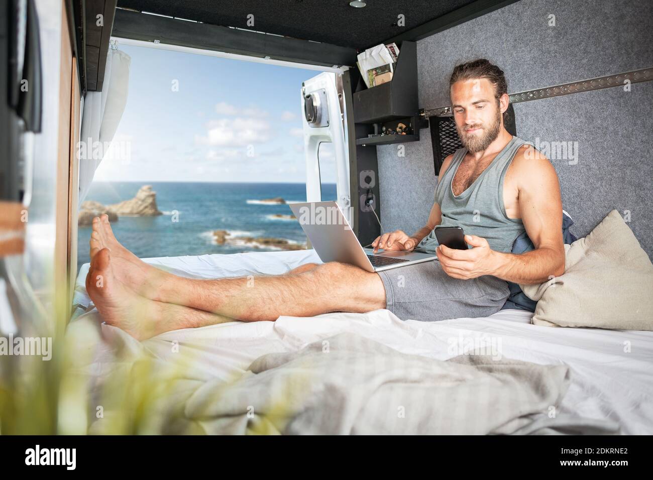 Man inside a camper van using laptop and smartphone Stock Photo