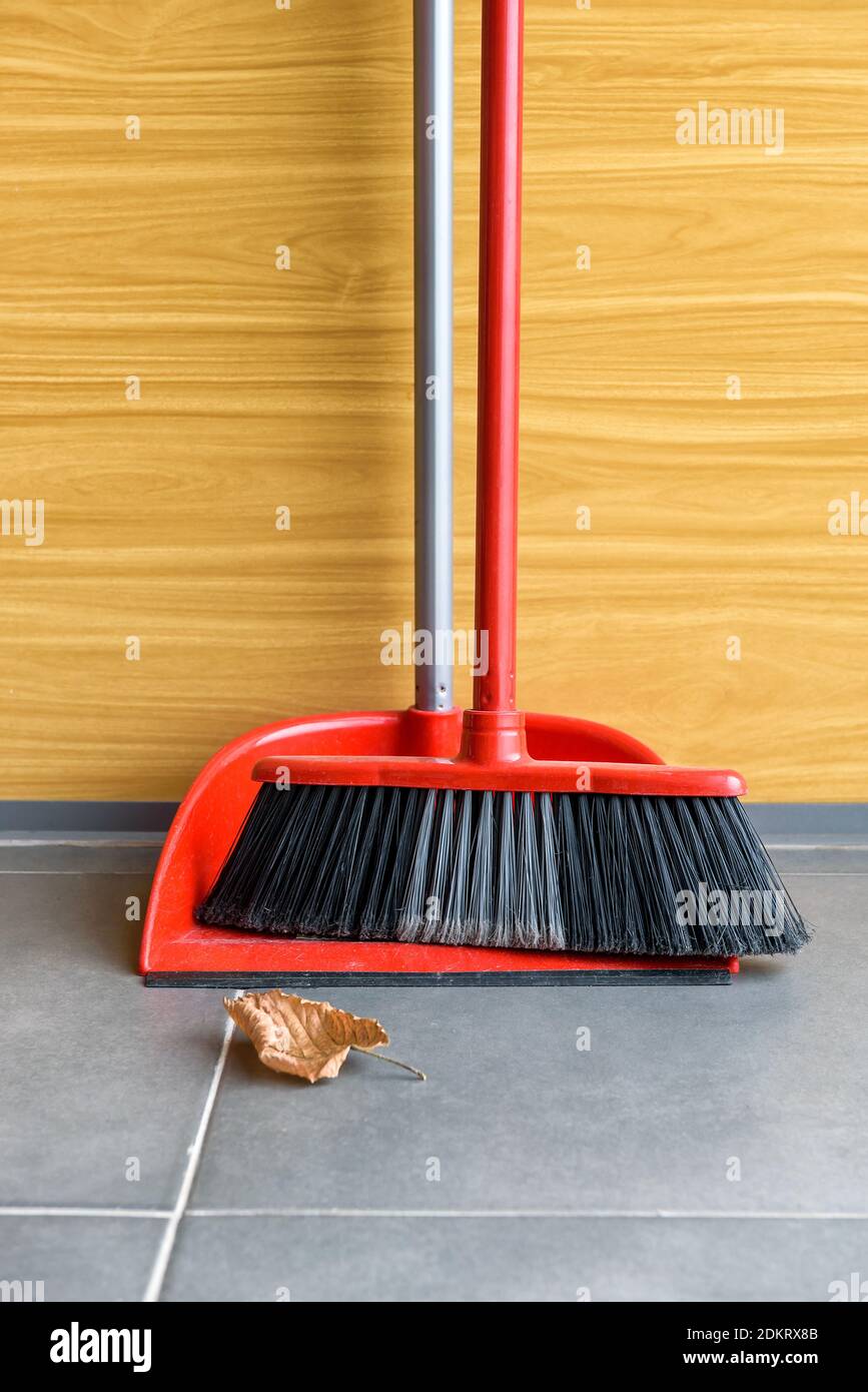Red handled broom with red dustpan for cleaning stand near the wall