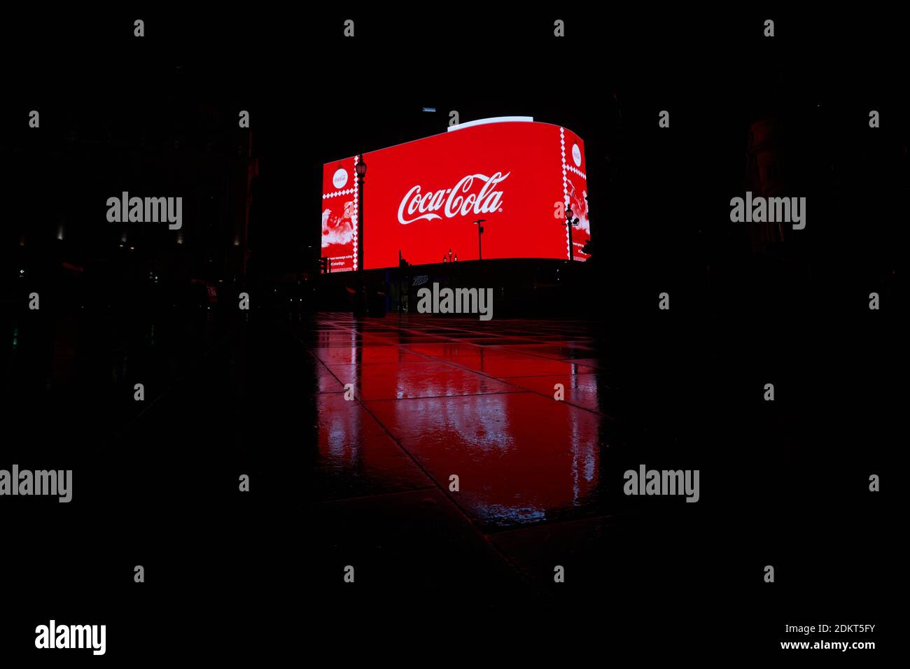 London, UK. - 15 Dec 2020: A Coco-cola advert on the giant illuminated billboard at Piccadilly Circus reflected on a wet pavement on the road opposite. Stock Photo
