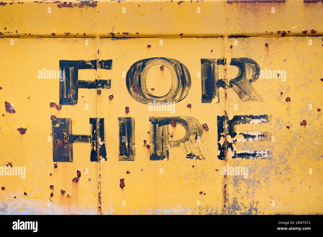 A close up of an old faded and rusted For Hire sign on the back of a junk yard heavy machine in Australia Stock Photo