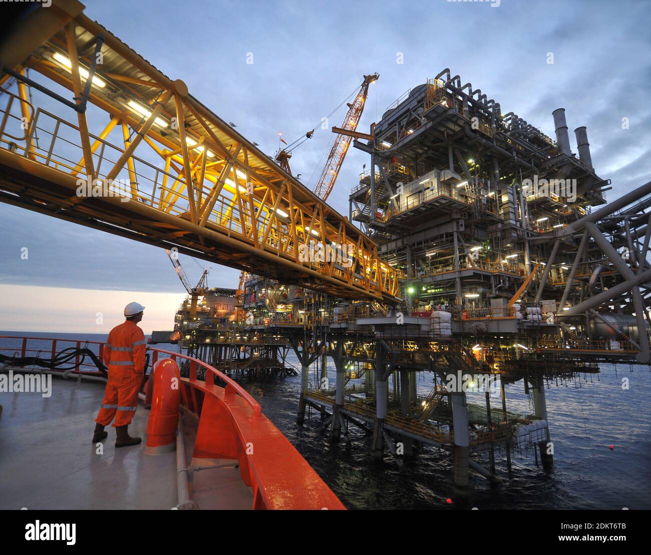 Offshore worker in full PPE stands on the deck of the Edda Fides support vessel with crossover bridge alongside a Bass Strait production Platform. Stock Photo