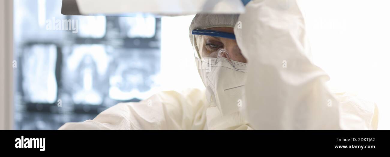Tired infectious disease doctor in respirator and protective overalls siting on floor with an X-ray image in hand in clinic Stock Photo