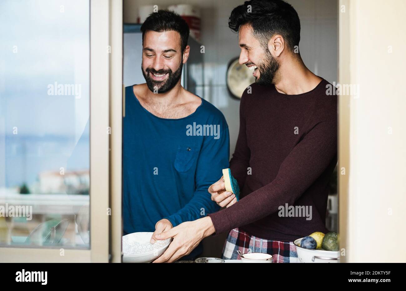 Young gay multiethnic couple, having cosmetic procedures, with black  patches and facial mask, working on a laptop at home. African man hugs his  friend from back. Home routine and work online Stock