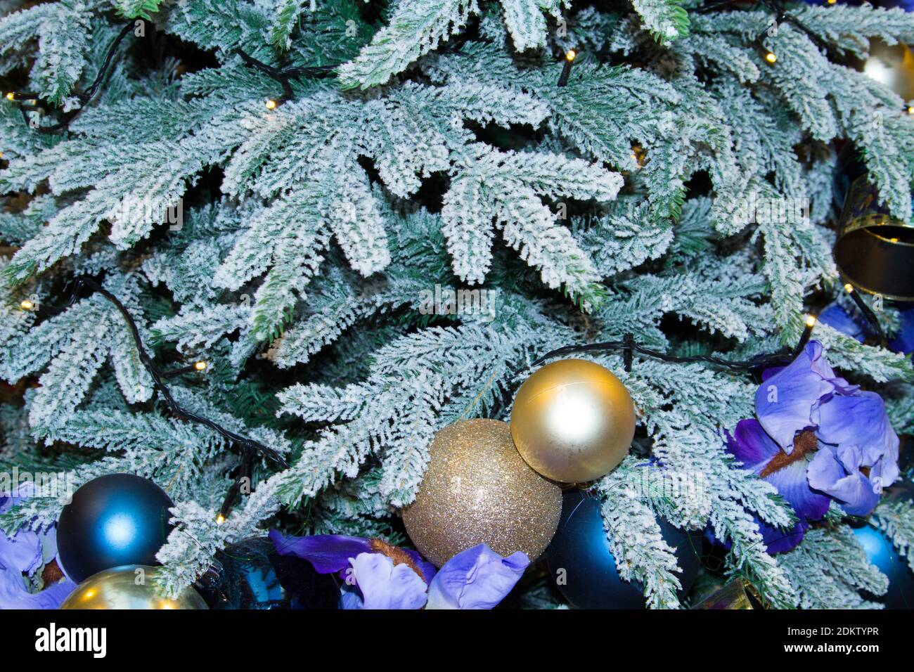Snow-covered artificial fir tree with Christmas decorations in the form of purple flowers and balloons. Stock Photo
