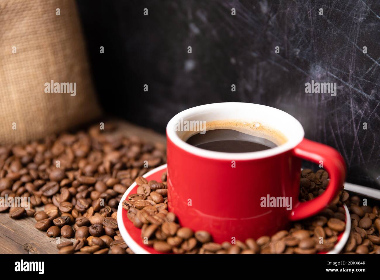Red cup of coffee with coffee beans on dark textured background. Morning fresh energy concept. Stock Photo