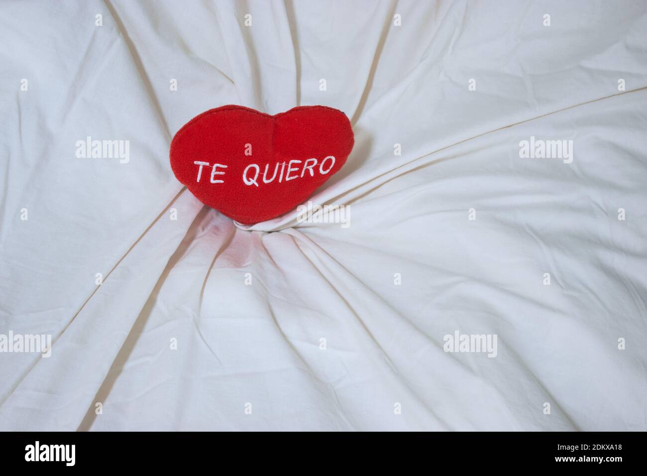 Red heart with embroidered text 'Te quiero'. Pillow cushion on bed of a couple in love. Valentine's Day concept 2021. Stock Photo
