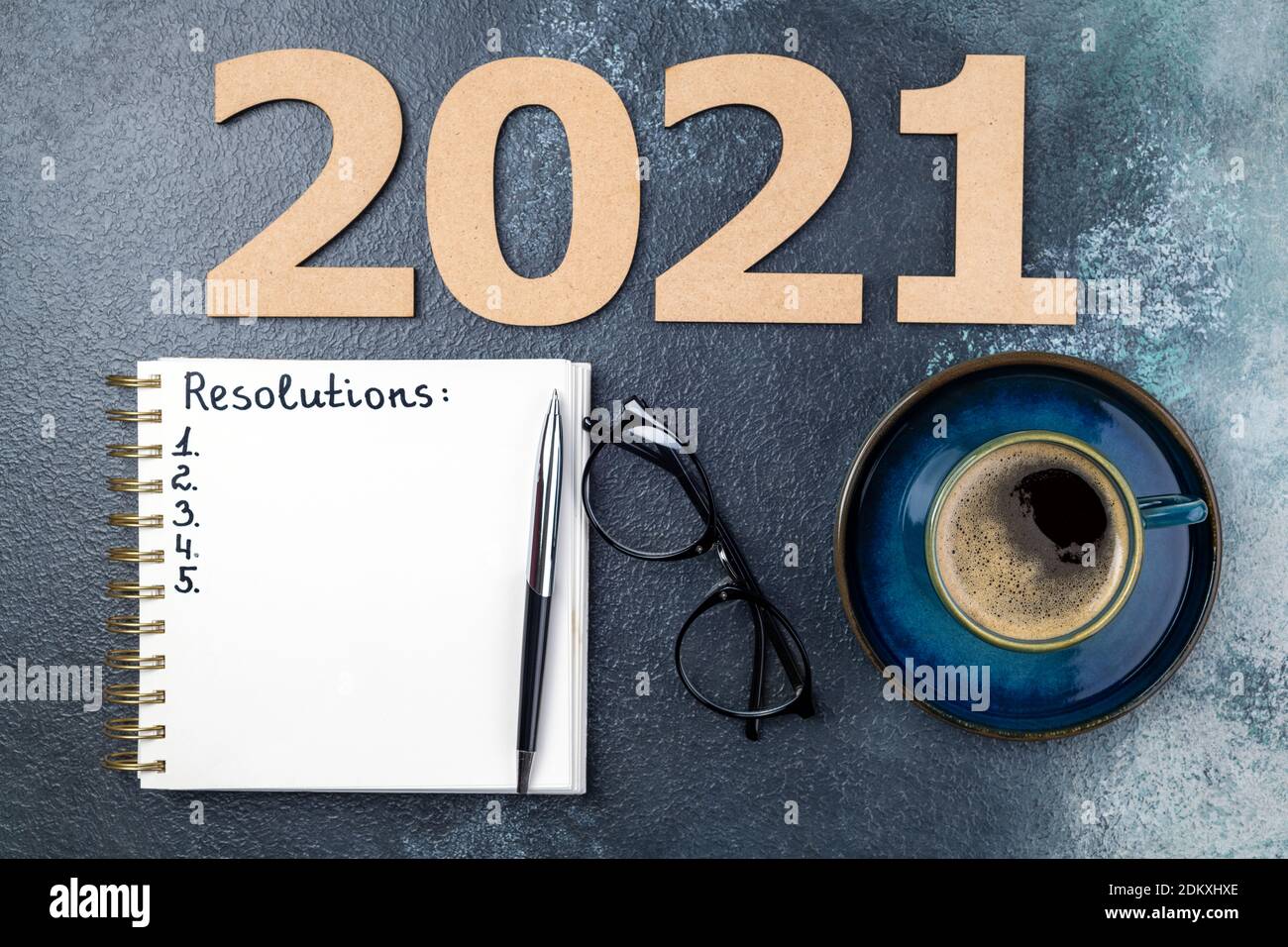 New year resolutions 2021 on desk. 2021 resolutions with open notebook, coffee cup, eyeglasses on blue background. Resolutions, goals, planning, strat Stock Photo