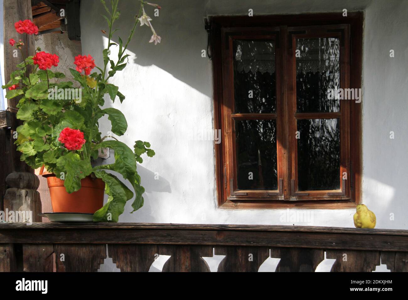 Vrancea County, Romania. Wooden frame window of an old traditional house. Potted flowers on the wooden porch. Stock Photo