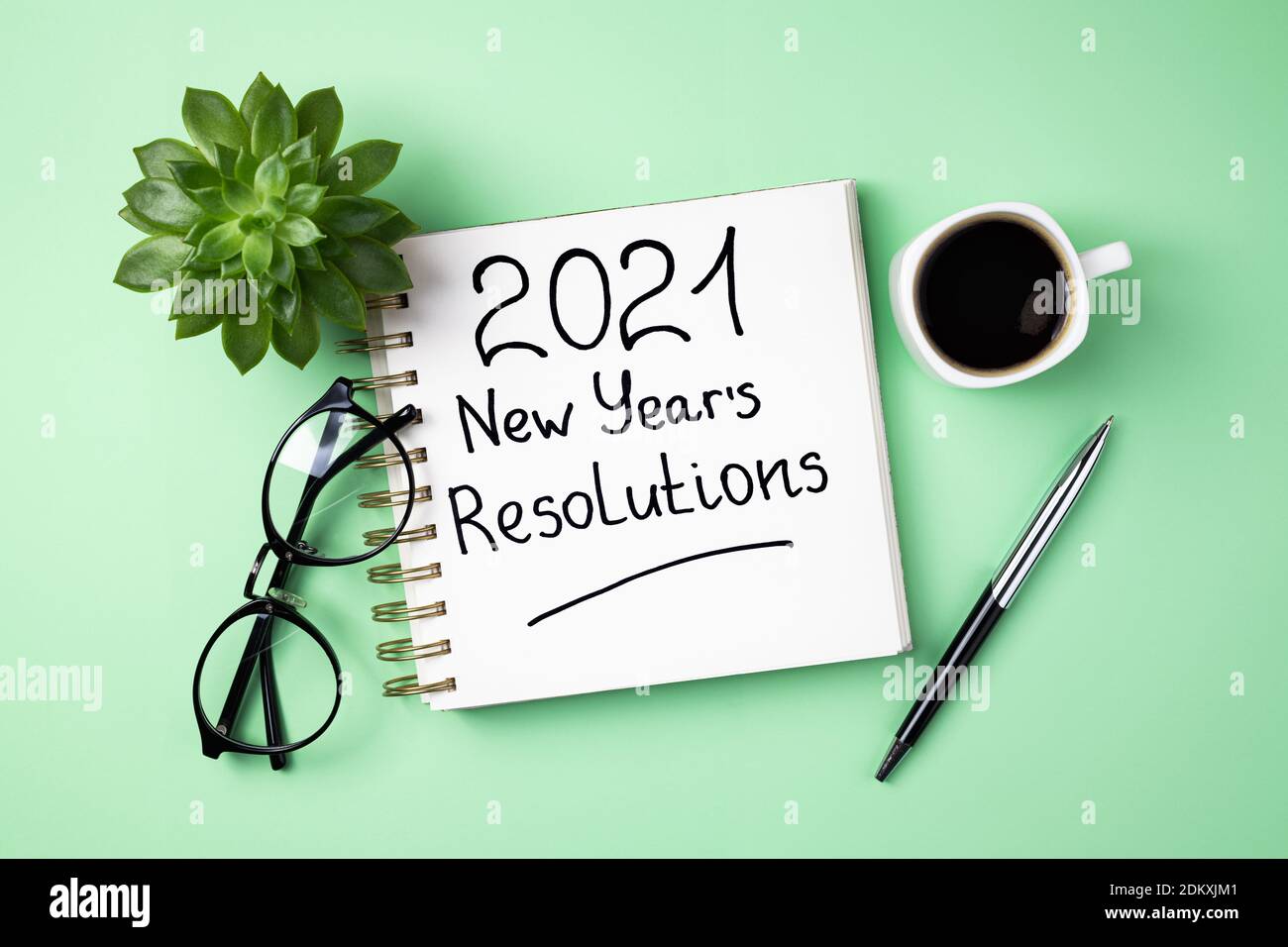 New year 2021 goals on desk. 2021 goals with open notebook, coffee cup, eyeglasses, plant succulent on green background. Goals, resolutions, plan, str Stock Photo