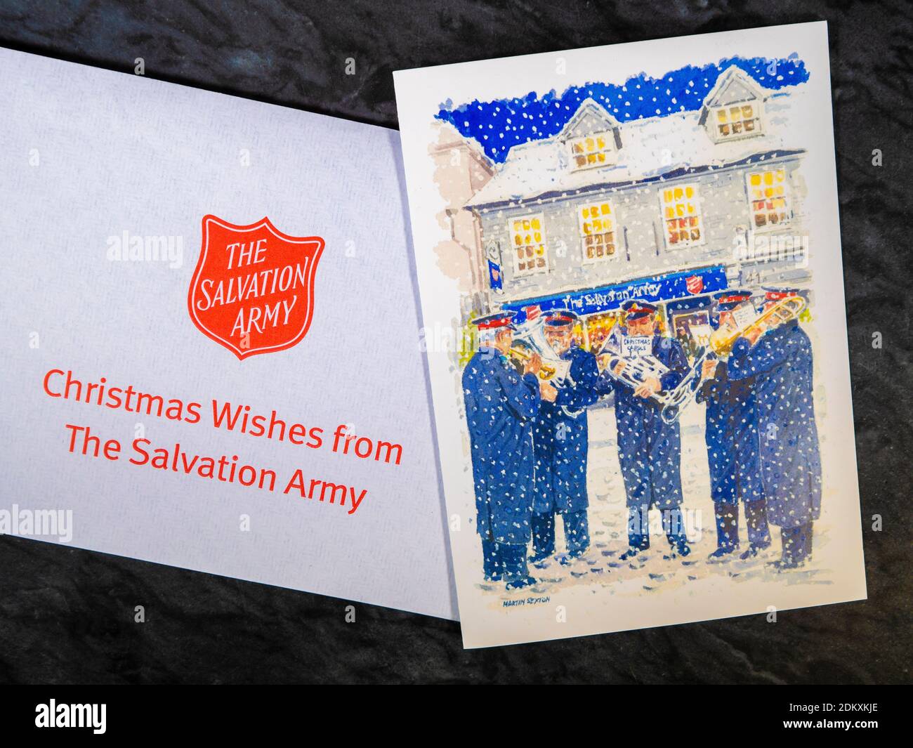 Closeup POV overhead shot of a plain envelope bearing the message Christmas Wishes from The Salvation Army, next to a seasonal British Christmas card. Stock Photo