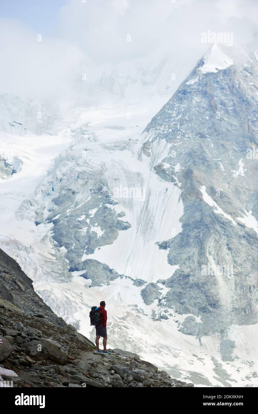 Vertical snapshot of incredibly beautiful mountain in Swiss Alps. Man tourist standing on a slope enjoying a cold quiete scenery. Concept of freedom, mountain hiking, tourism and alpinism Stock Photo