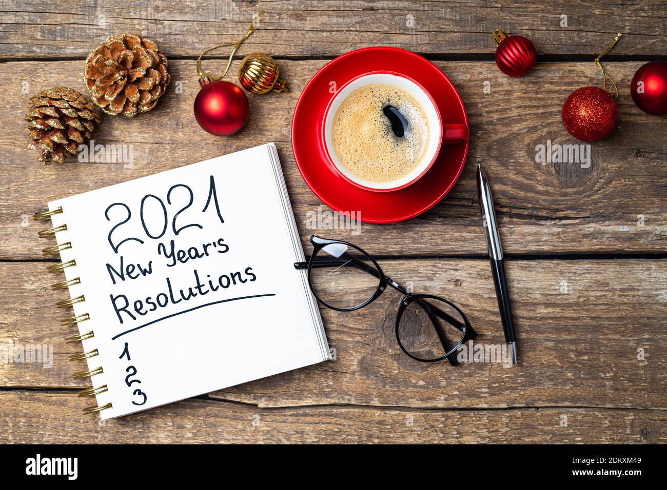 New year 2021 resolutions on desk. 2021 goals with notebook, coffee cup, eyeglasses, Christmas ornaments on wooden background. Goals, plan, strategy, Stock Photo