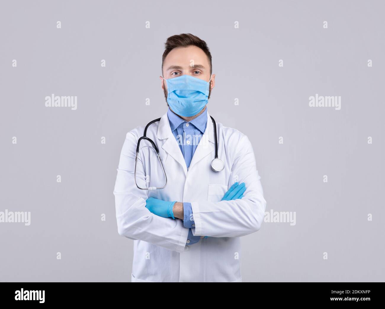 Professional male doctor in uniform, face mask and rubber gloves posing over grey studio background Stock Photo