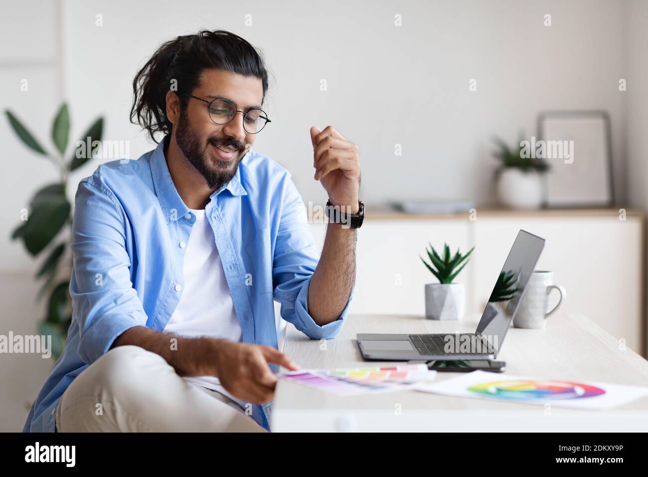 Arab Graphic Designer Working With Color Swatches And Laptop At Home Office Stock Photo