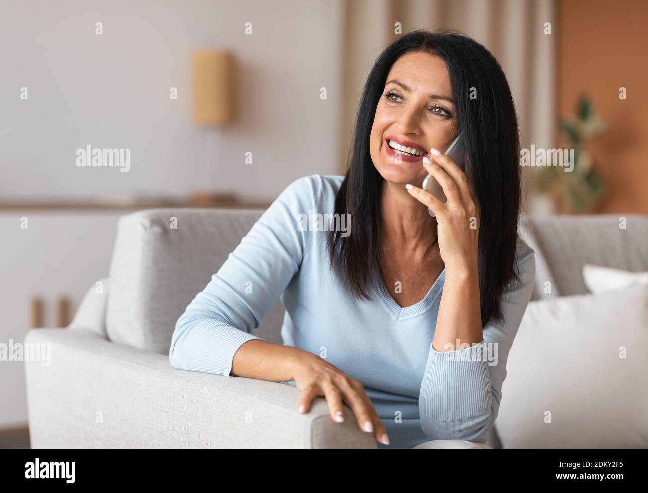 Smiling mature woman talking on cellphone sitting on sofa Stock Photo ...