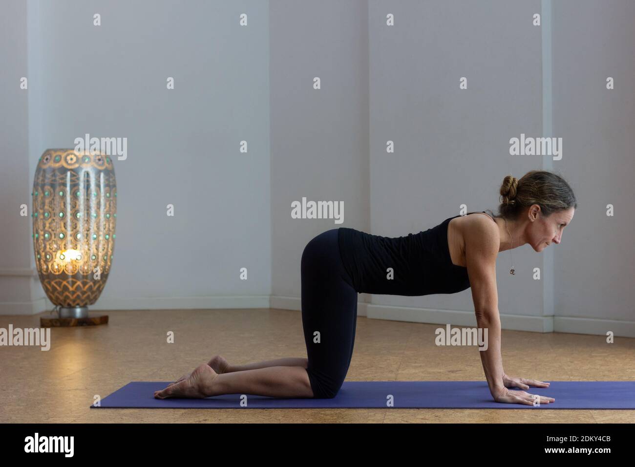 Slim woman practices yoga in bitilasana posture in studio. Female yogi in cow pose indoors. Staying fit, workout session at home concepts Stock Photo