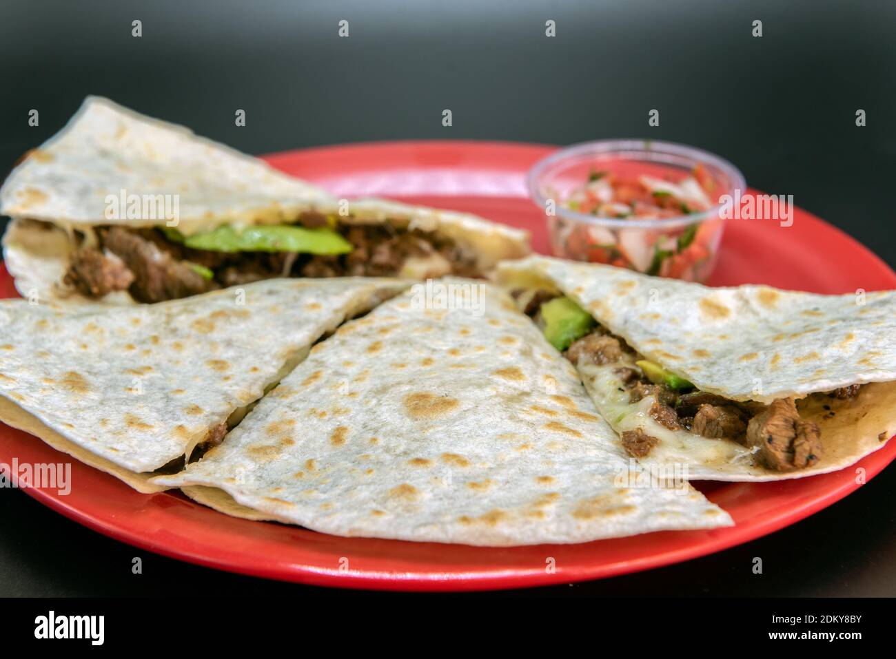 Steak Asada quesadilla loaded with fresh meat, melted cheese and cut in wedges and presented on a red plate. Stock Photo