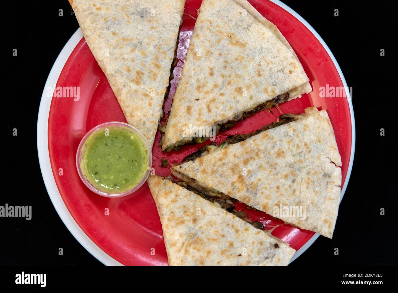 Overhead view of veggie quesadilla loaded with fresh vegetables, melted cheese, and flour tortilla and presented on a red plate. Stock Photo