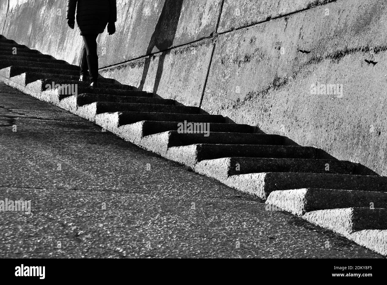 Silhouette of woman walking up steps near seawall during lockdown in black and white Stock Photo