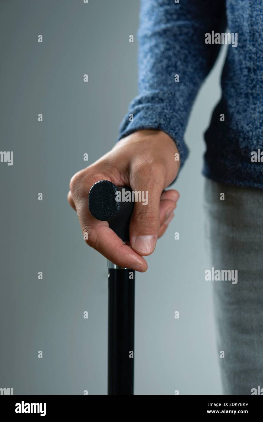 closeup of a caucasian man using a walking stick with a black handle, on a gray background Stock Photo