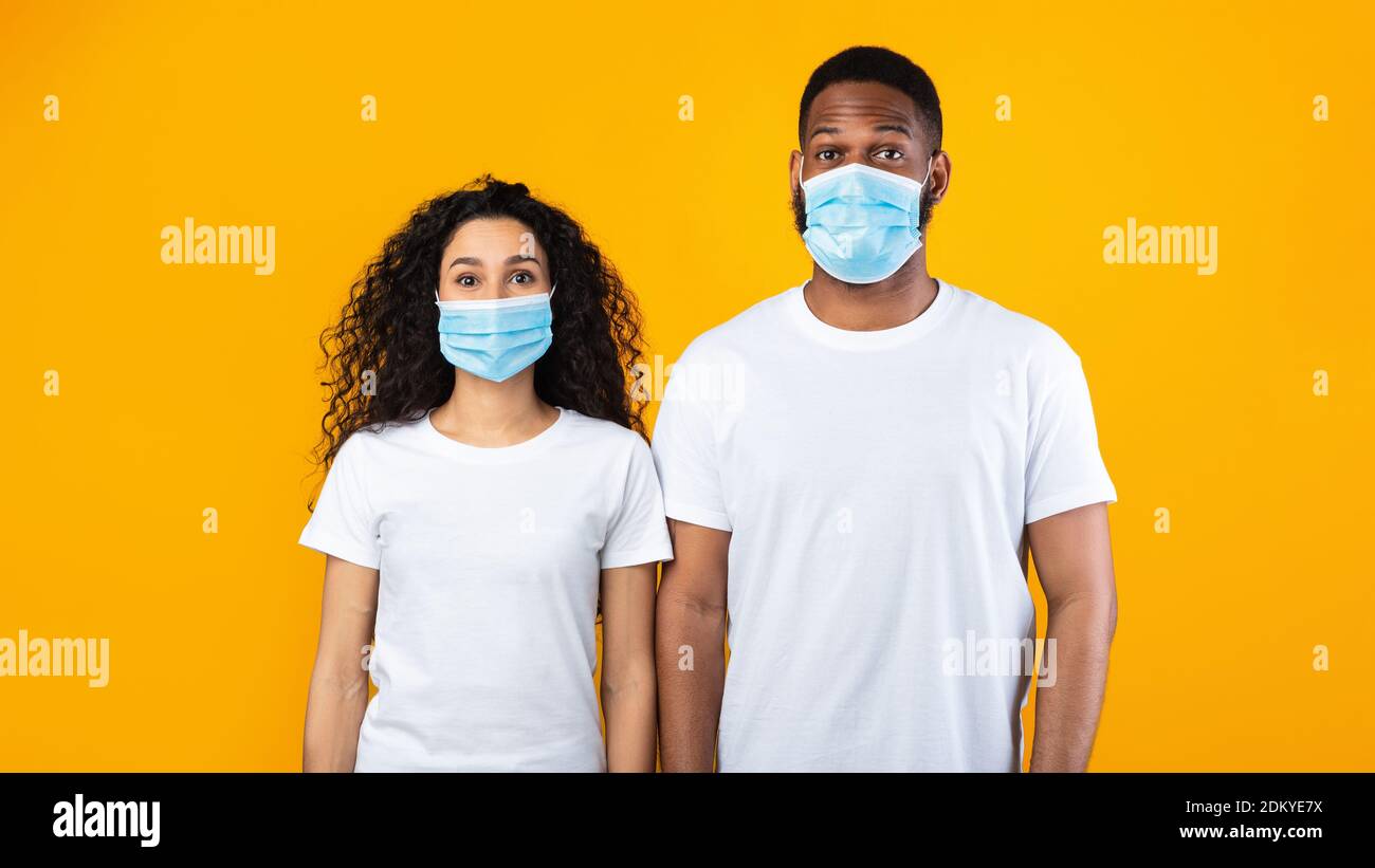 Multiethnic Couple Wearing Face Masks Posing Over Yellow Studio Background Stock Photo