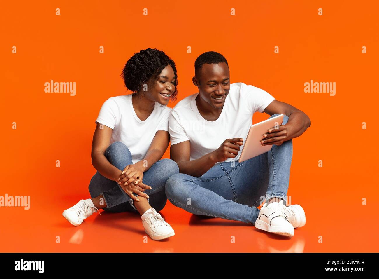 Cheerful black couple using digital tablet over orange Stock Photo
