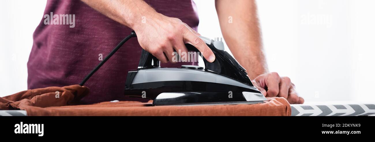 Cropped view of man ironing clothes on board at home, banner Stock Photo