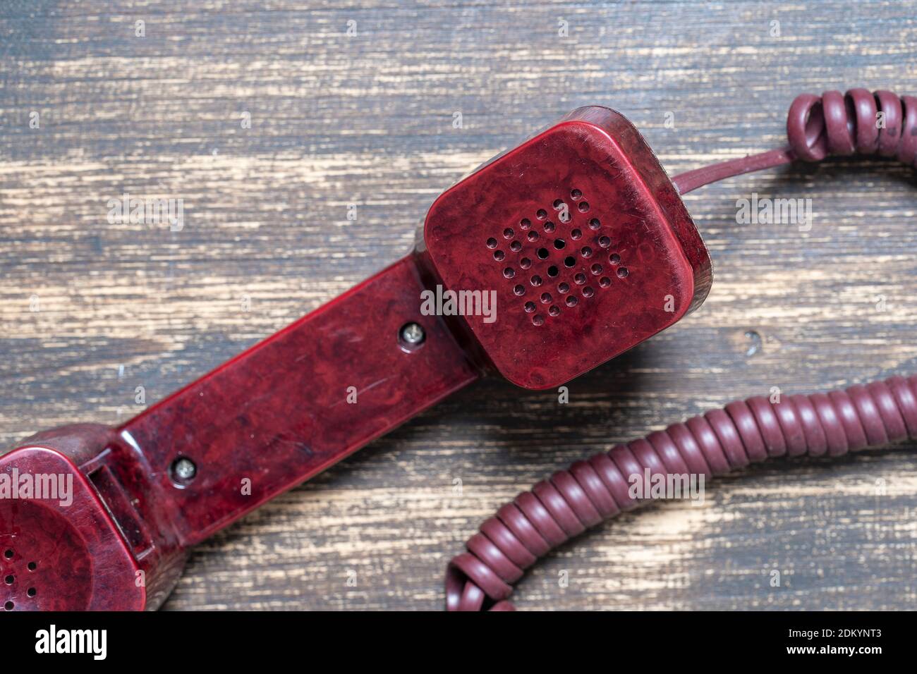 Vintage red old telephone receiver with cord on a wooden board, close