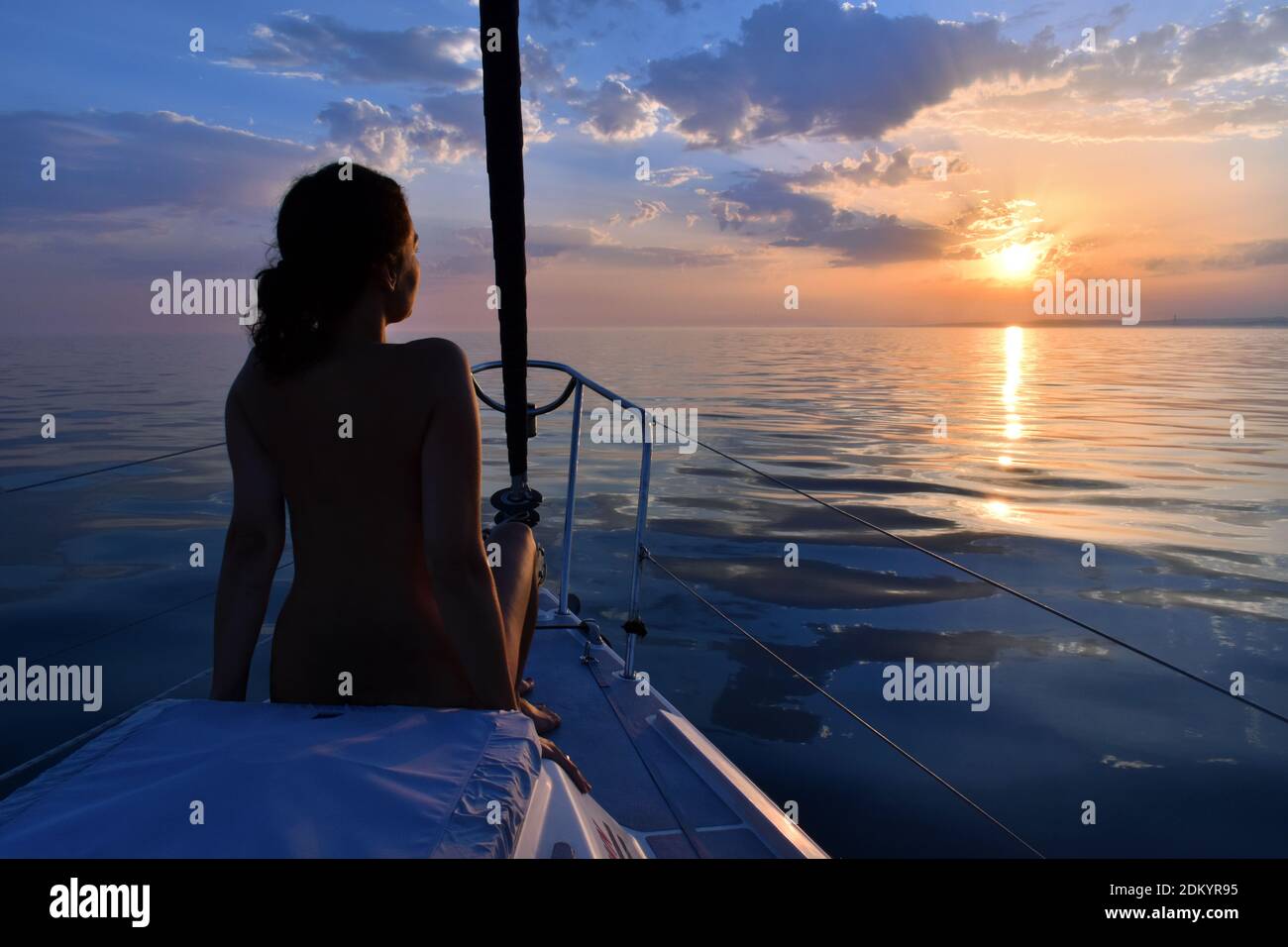 Woman relaxing on sailboat during serene sunset at sea Stock Photo