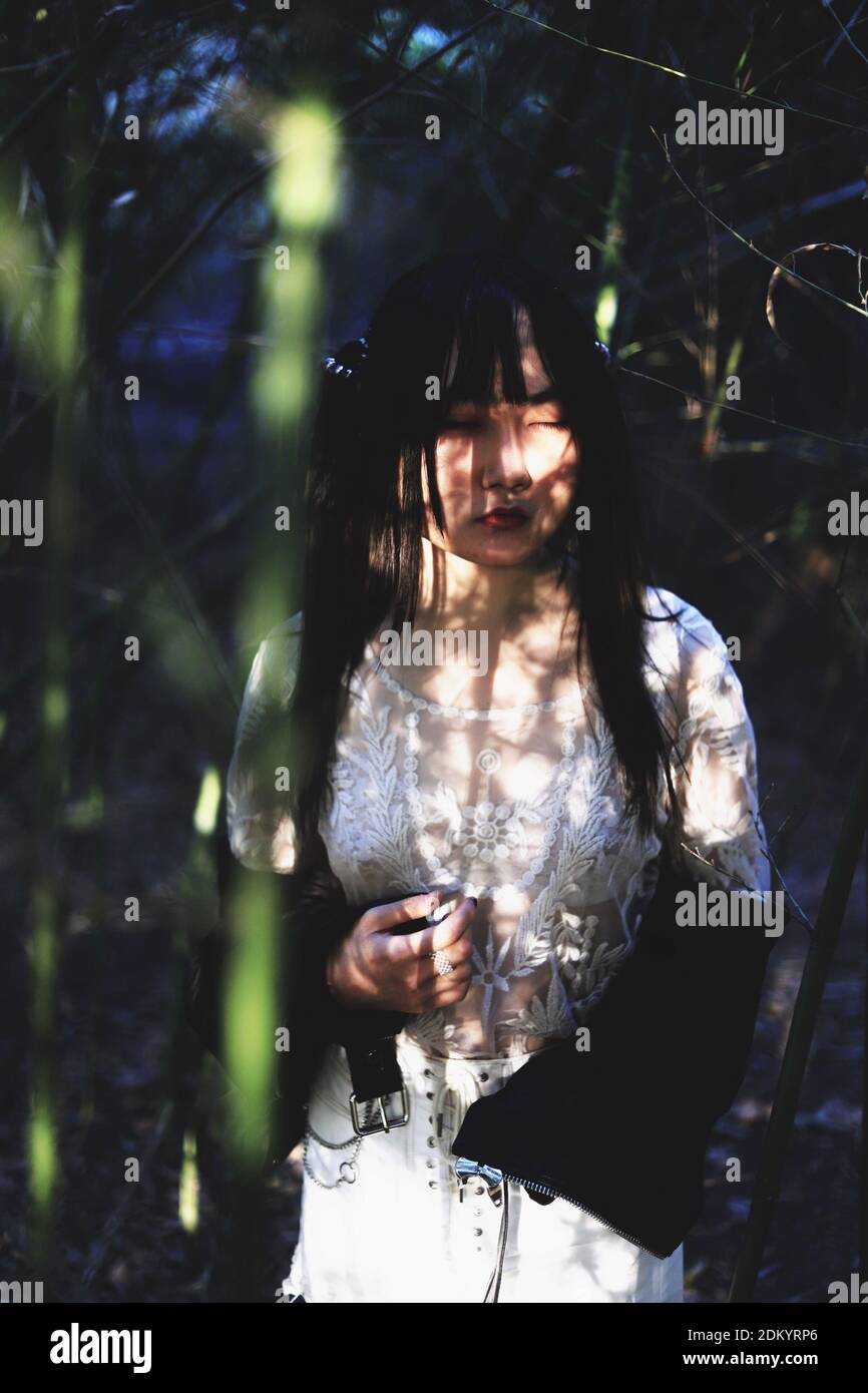Young Woman Looking Away While Standing Against Plants Stock Photo