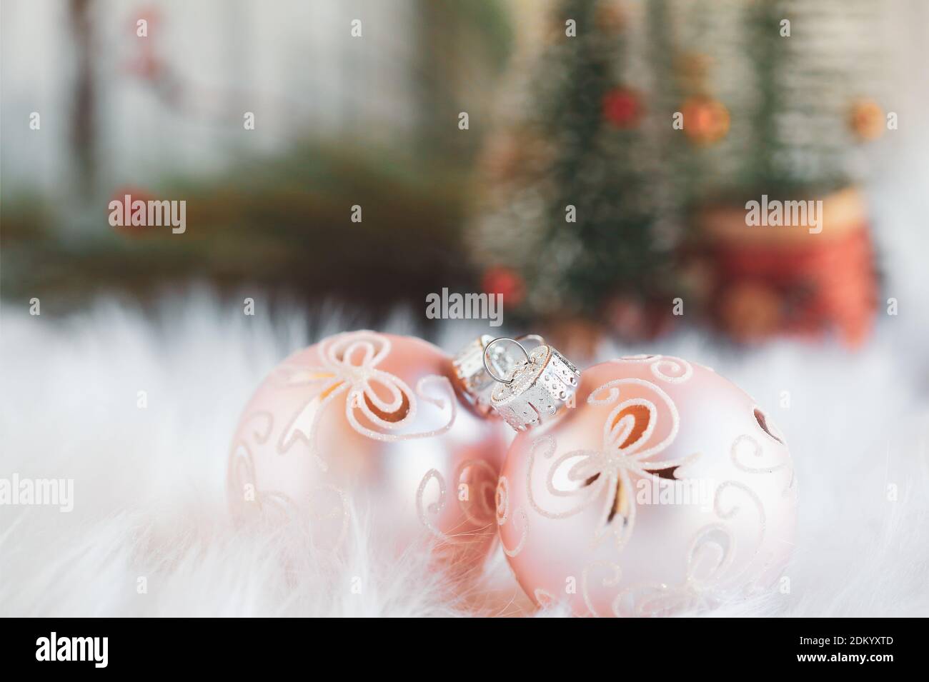 Two pink Christmas ornaments lying on a white rug. Selective focus with Christmas trees blurred into the background. Stock Photo