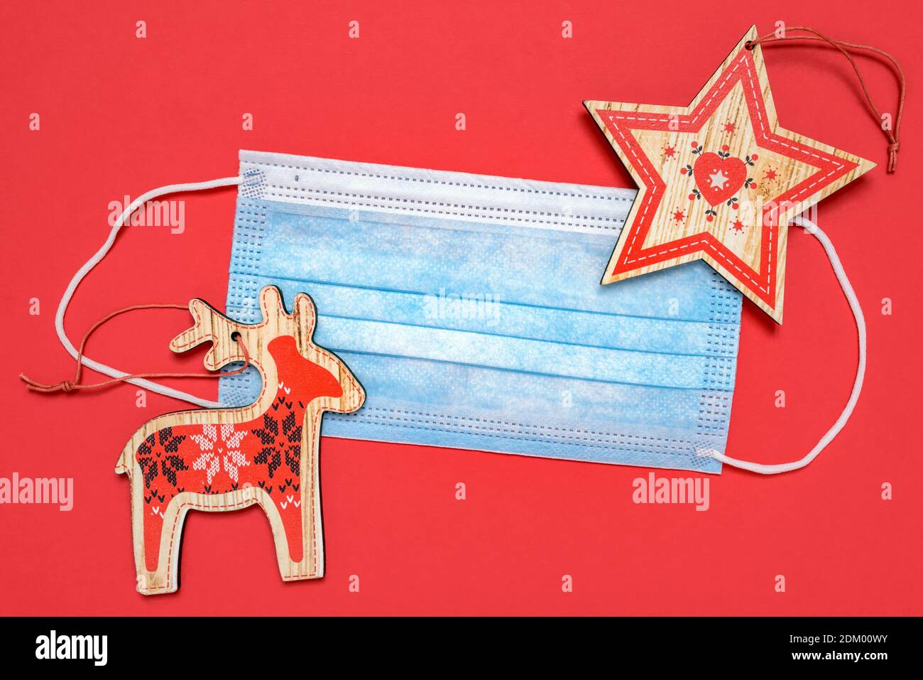 Medical mask and decorative Christmas ornaments on red background. The concept of celebrating the New Year and Christmas during the COVID-19 epidemic. Stock Photo