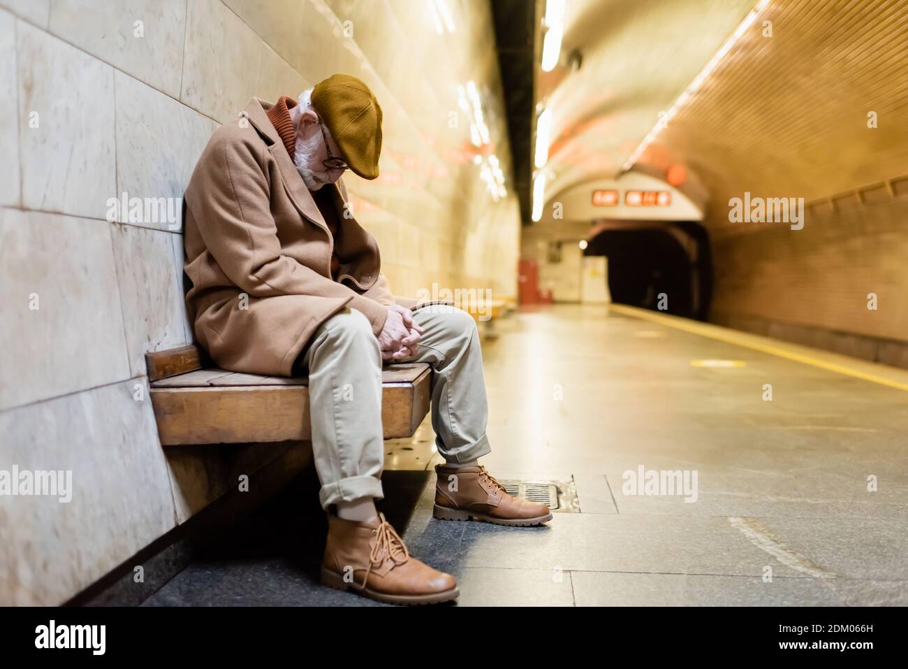 elderly man in autumn outfit sleeping on subway platform bench Stock Photo
