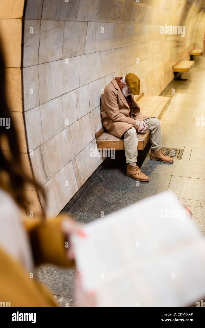 senior man in autumn outfit sleeping on metro platform bench on blurred foreground Stock Photo