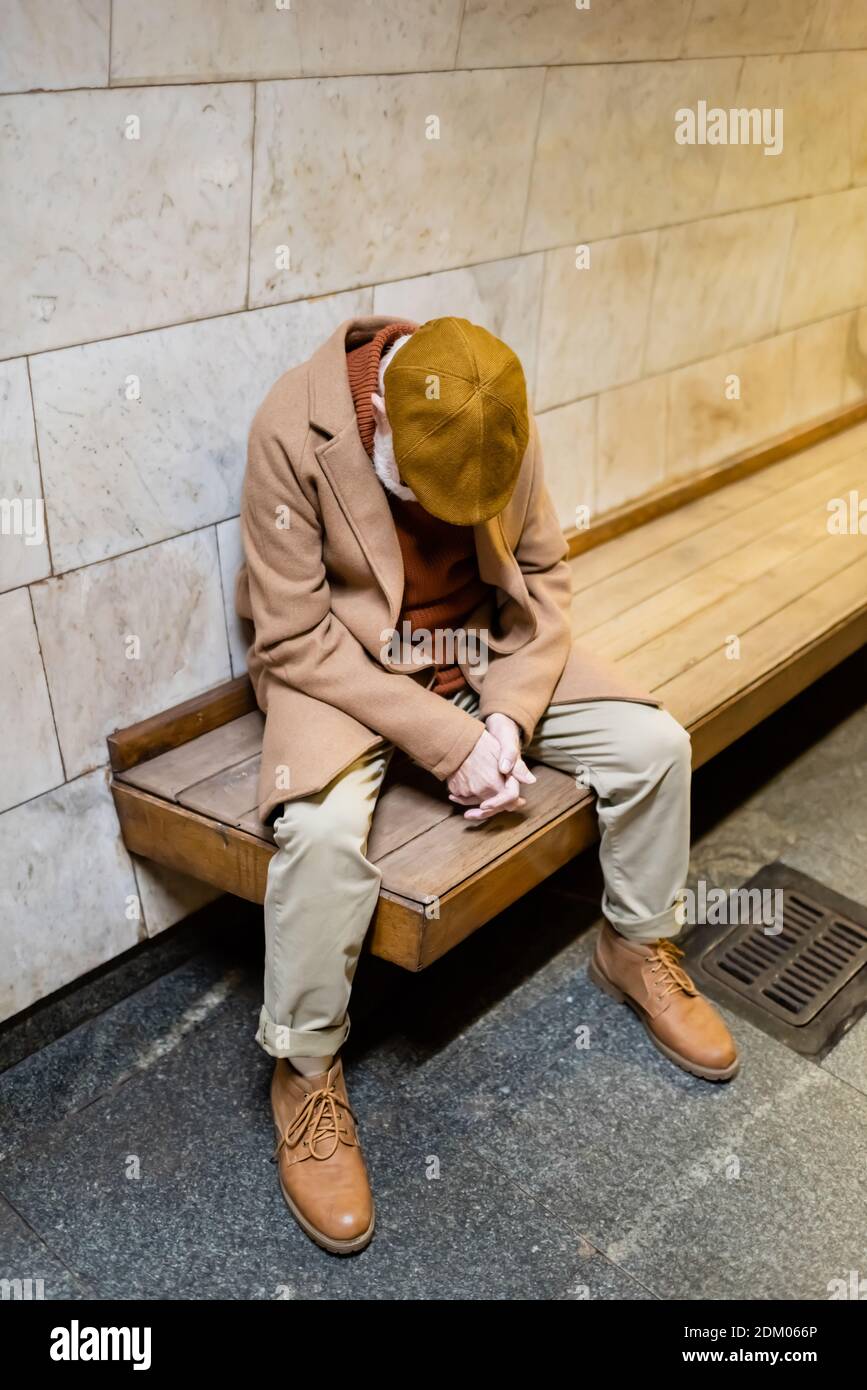 aged man in autumn coat and cap sleeping on underground platform bench Stock Photo