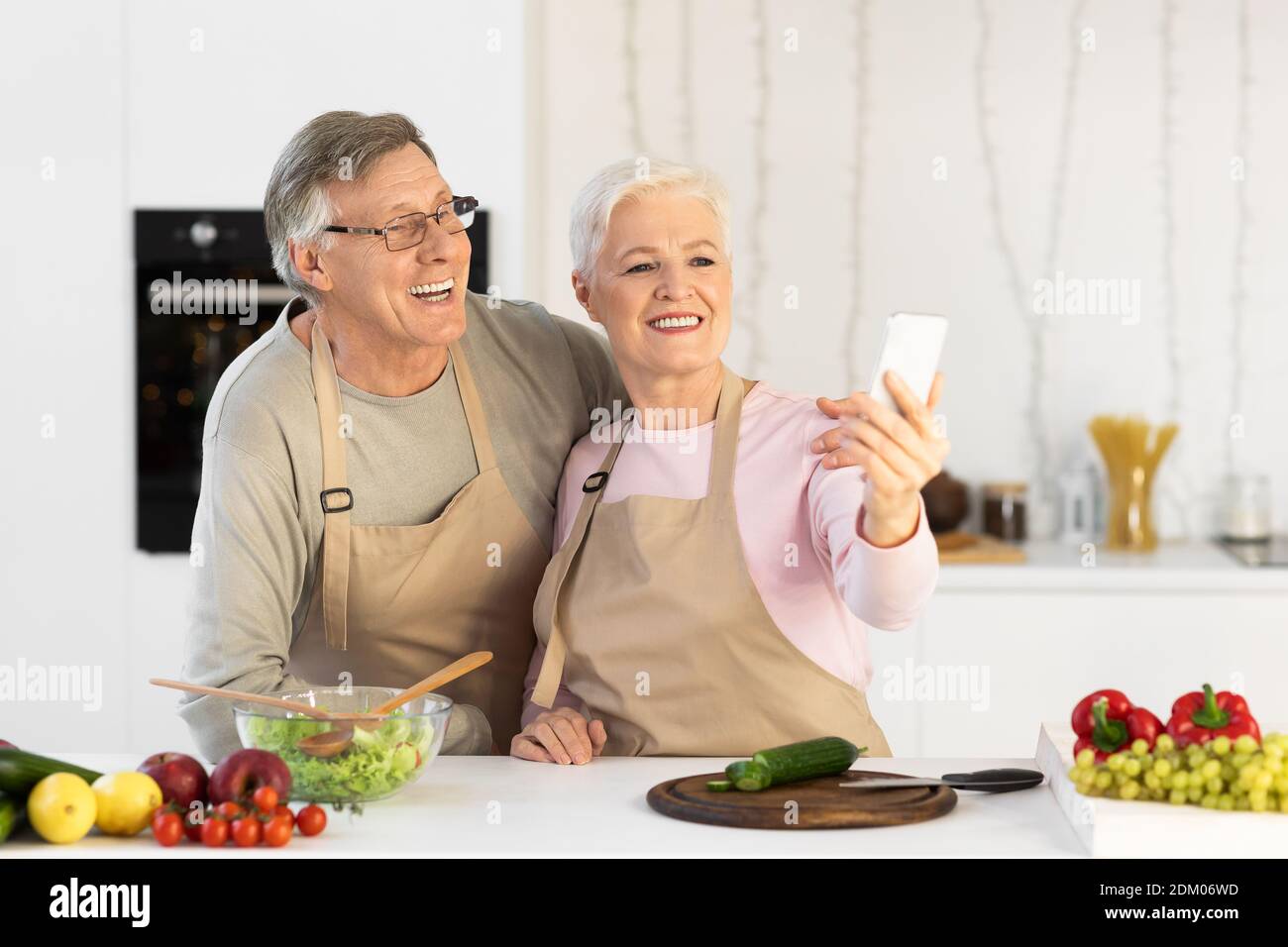 Joyful Elderly Spouses Making Selfie Having Fun Cooking In Kitchen Stock Photo