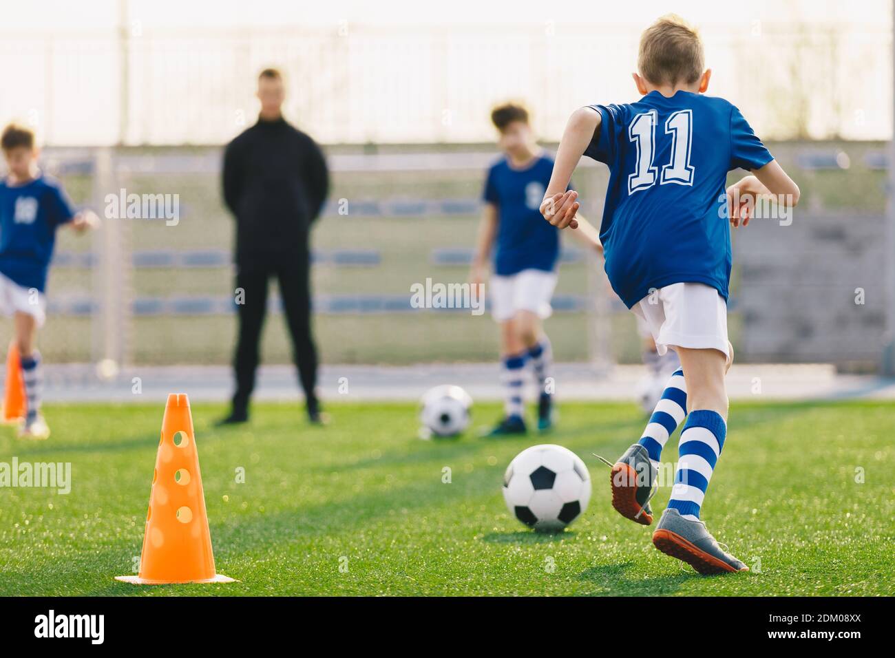 Group of young boys with coach practicing soccer on field. Kids running football balls on