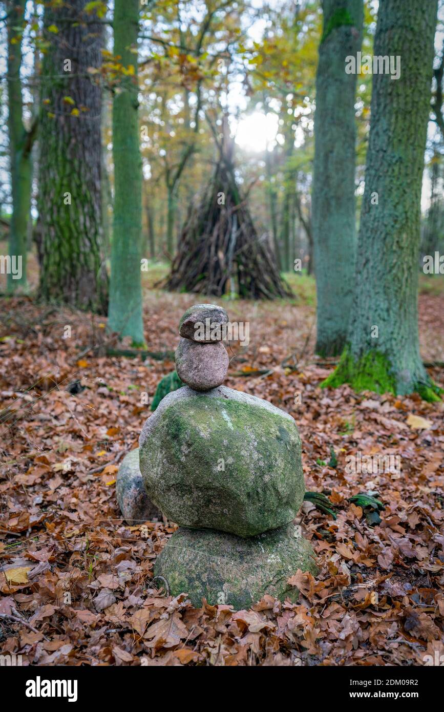 Mystical shot of a stone cairn in the woods with a wooden stack of branches in the background Stock Photo