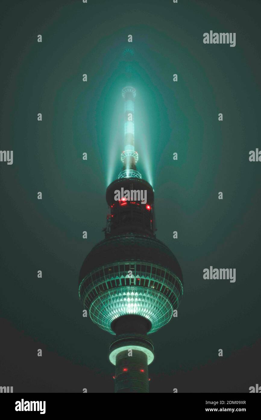 Scenic View Famous Alexanderplatz TV Tower of Berlin, Germany in Colorful Turquise Color surrounded by Fog at Night, Close up View of Antenna Stock Photo