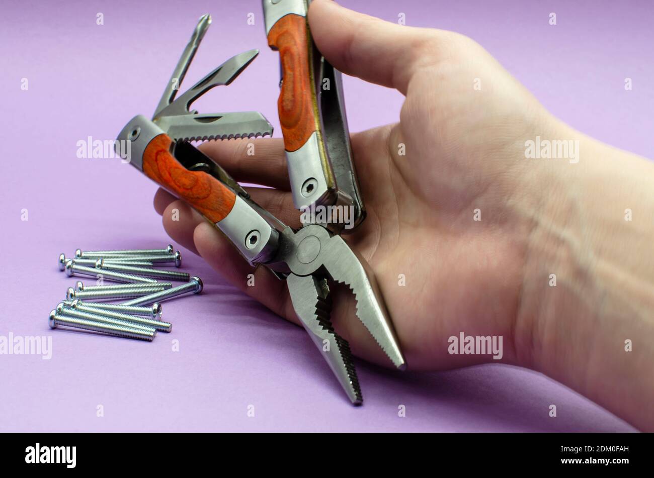 multitool turned into pliers, knife, screwdriver in the hand on violet background, screw