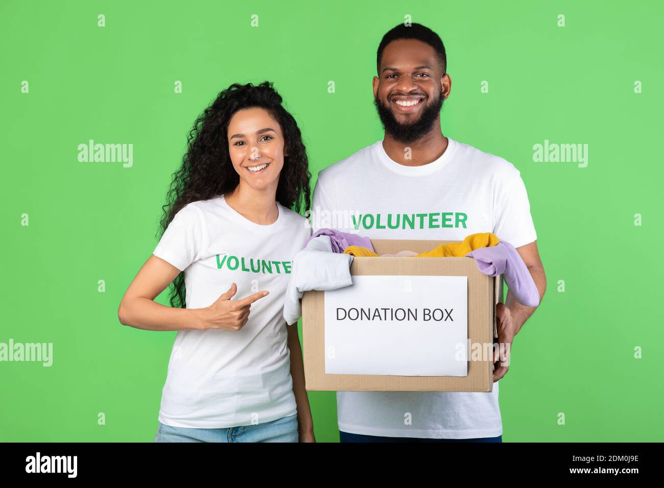 Two Volunteers Holding Donation Box Standing Over Green Background Stock Photo