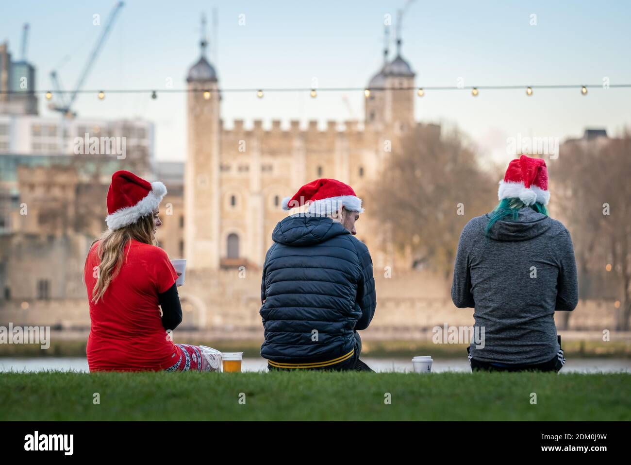Christmas 2020: Friends wearing Santa hats wait by The Queen's Walk promenade opposite Tower of London building in the afternoon light, London, UK. Stock Photo