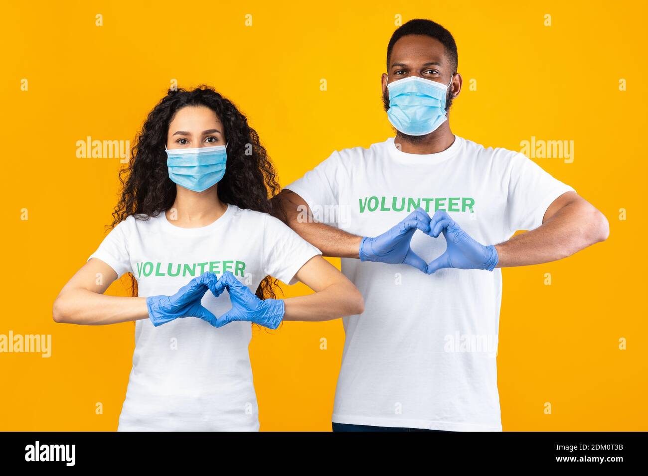Two Volunteers Gesturing Heart-Shape Wearing Masks And Gloves, Yellow Background Stock Photo