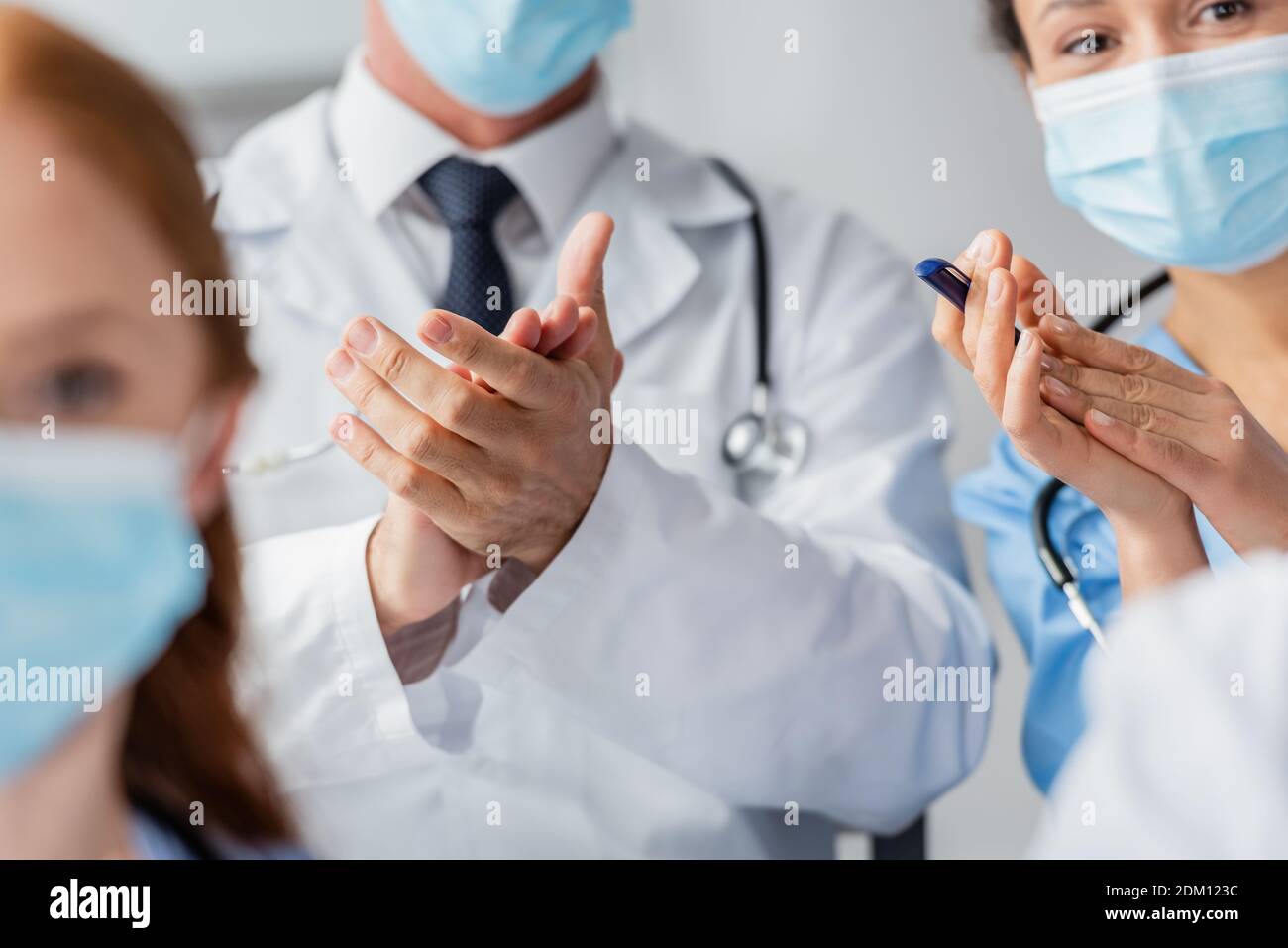 Multicultural doctor and nurse applauding during meeting with blurred ...