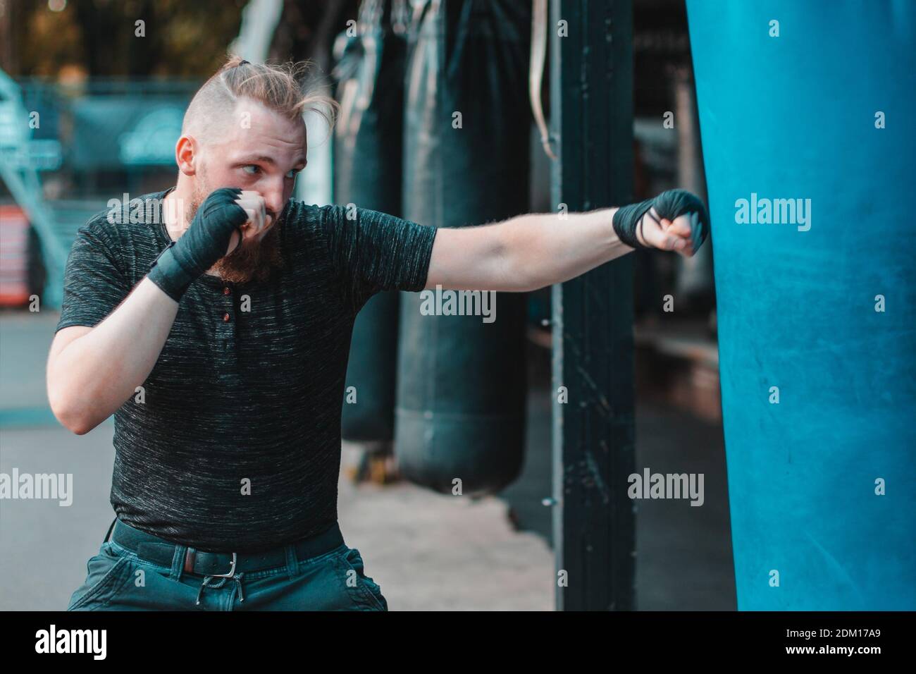 Street Fighter In Black Clothes And Bandages On The Wrist Boxing In Punching Bag Outdoors Young Man Doing Box Training And Practicing His Punches At The Outside Gym Stock Photo Alamy