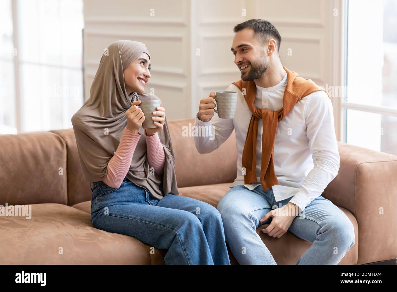 Happy Muslim Couple Drinking Coffee Sitting On Sofa At Home Stock Photo